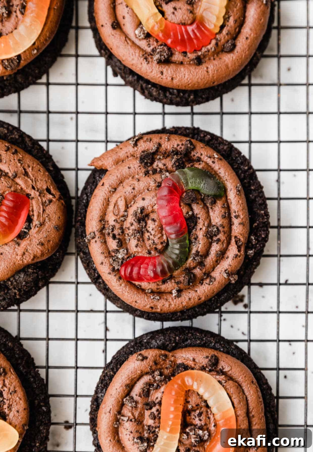 Oreo Mud Pie Cookies 11 Chocolate frosted Dirt Cake Cookies with Oreo crumbs and a gummy worm, on a wire cooling rack.