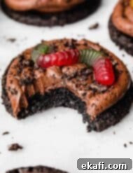 Oreo Mud Pie Cookies 13 A bite taken out of a chocolate frosting topped Dirt Cake Cookie with a garnish of Oreo crumbs and a gummy worm.
