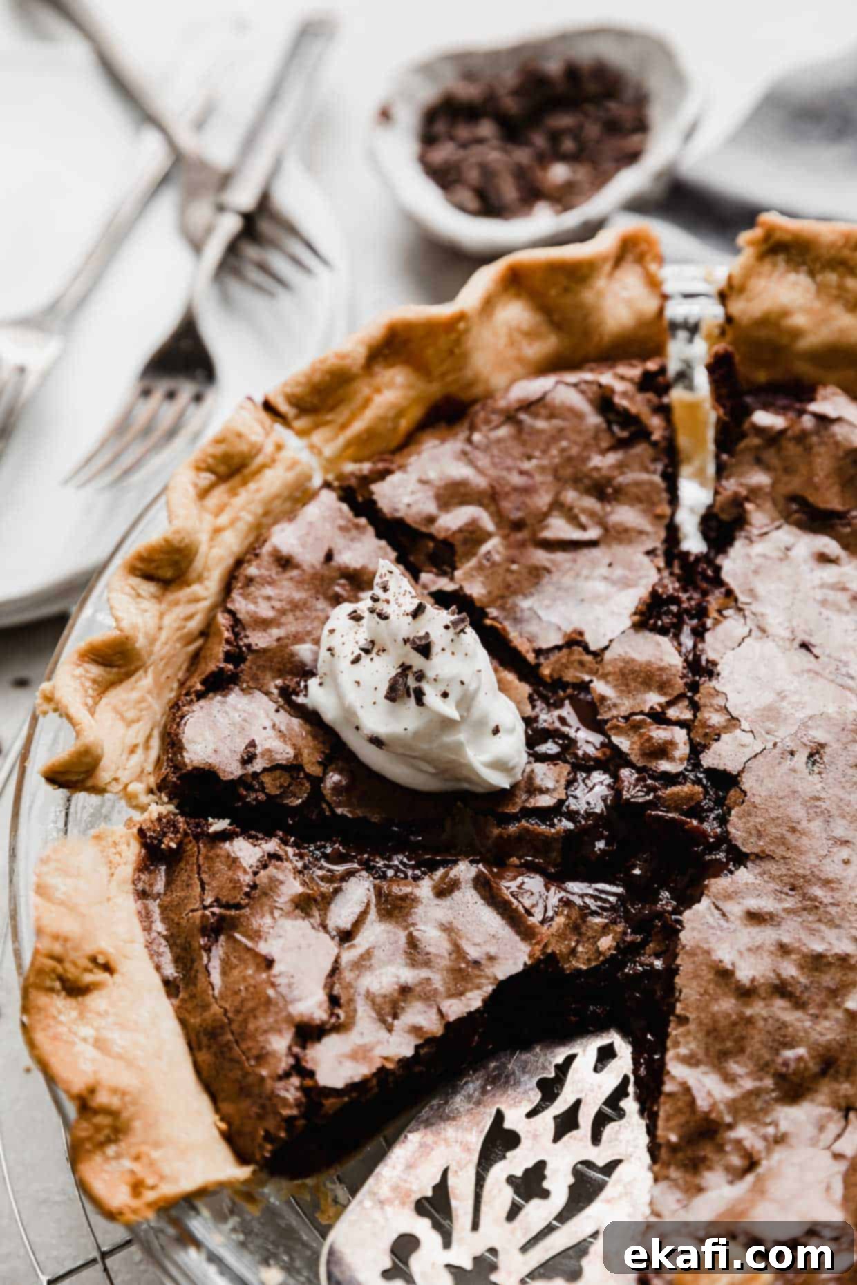 Καρυδόπιτα Μπράουνι 2 Μια Brownie Pie κομμένη σε φέτες, με μια φέτα καλυμμένη με λευκή σαντιγί και σοκολατένιες νιφάδες.