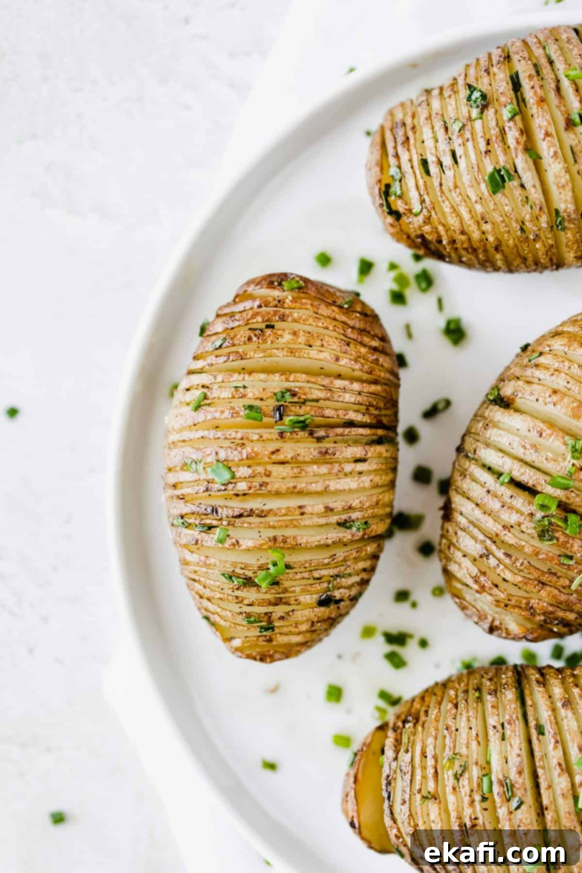 Hasselback potatoes are a fun way to enjoy a potato. The exterior is crisp and the interior is buttery, soft, and tender! A perfect side dish to any meal! Hasselback Potatoes topped with fresh chives on a white plate.