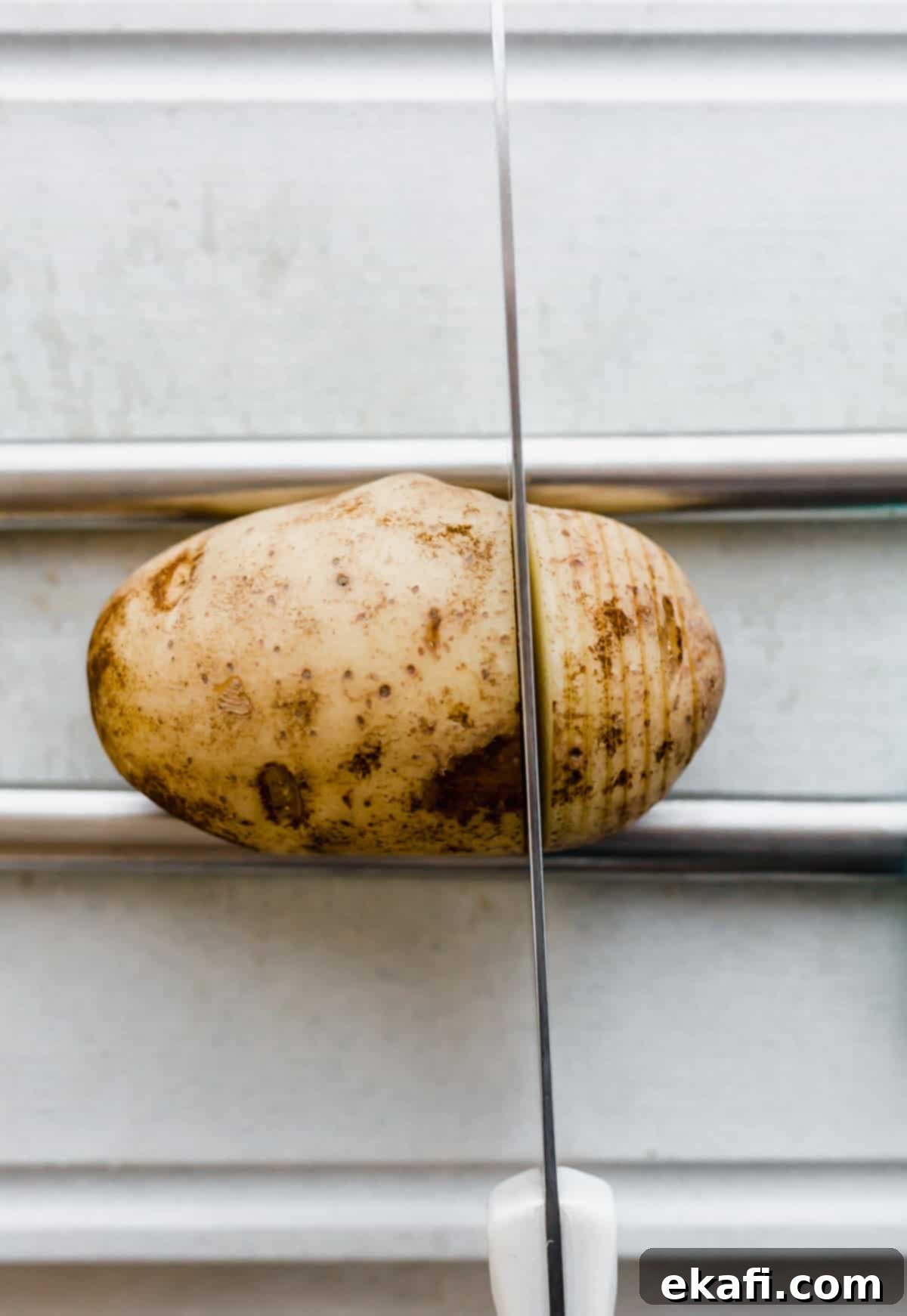 Hasselback potatoes are a fun way to enjoy a potato. The exterior is crisp and the interior is buttery, soft, and tender! A perfect side dish to any meal! A russet potato with a cutting knife cutting through the potato.