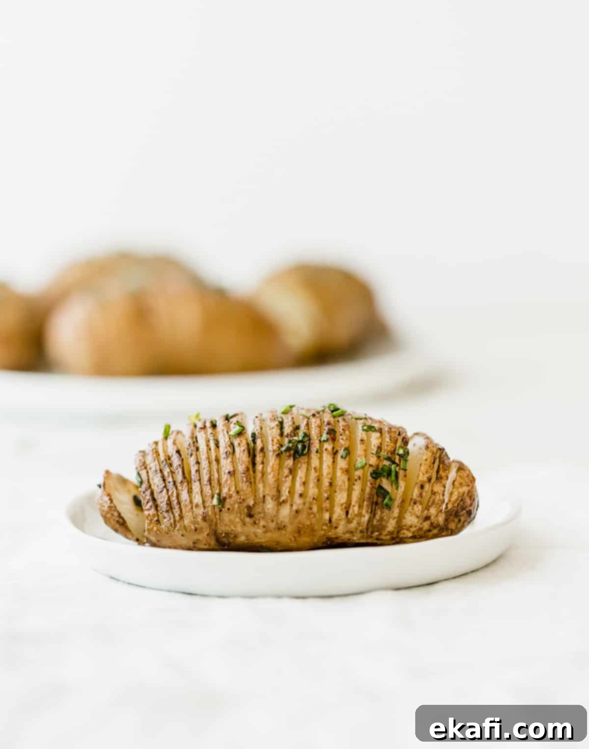 Crispy Air Fryer Hasselback Potatoes 6 A Hasselback Potatoe on a white plate against a white background.