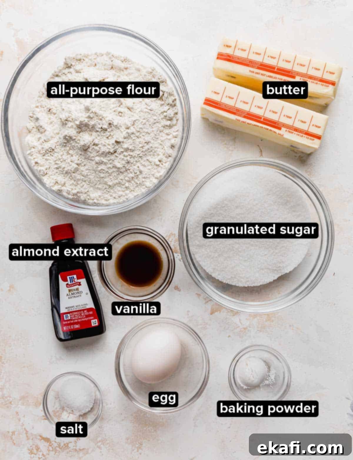 Frosted Sugar Cookie Bars 3 Sugar Cookie Bars ingredients portioned into glass bowls on a white textured background, showcasing fresh, quality components.