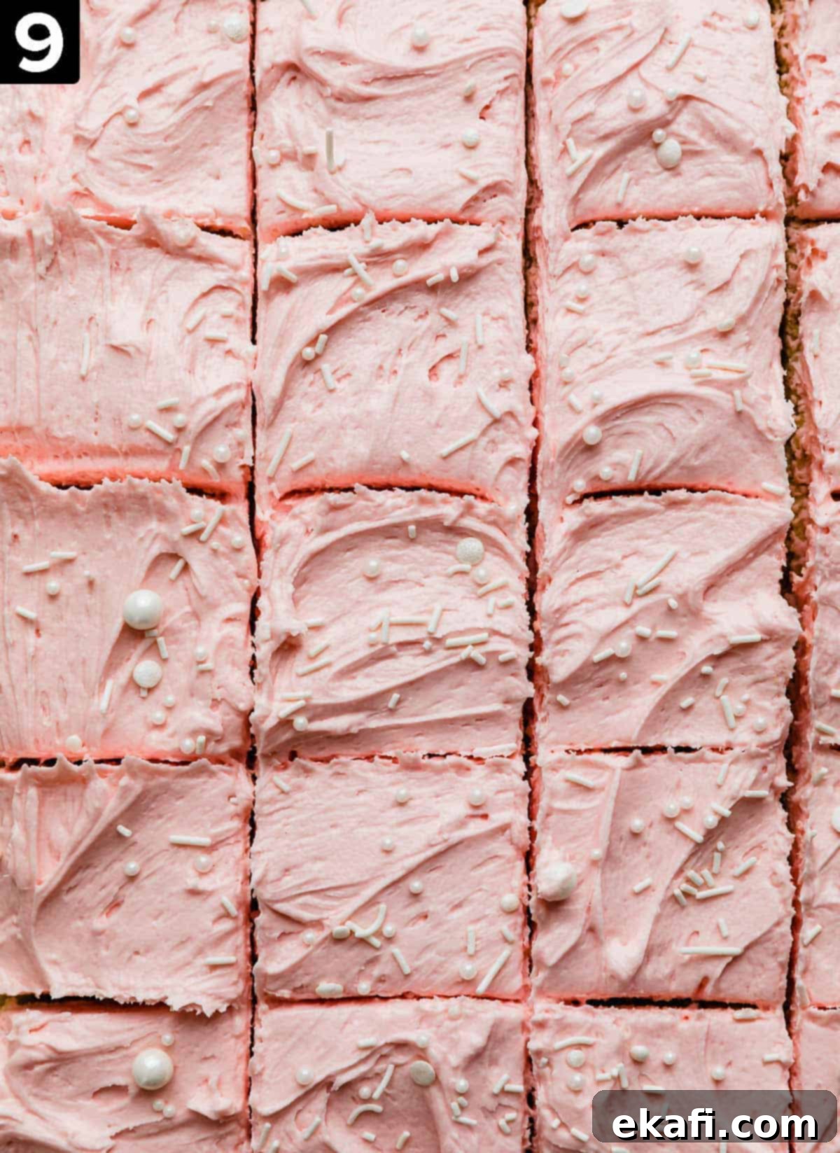 Frosted Sugar Cookie Bars 6 Pink frosting covered Sugar Cookie Bars topped with a sprinkling of white sprinkles, and the bars are cut into small squares, ready for enjoyment.