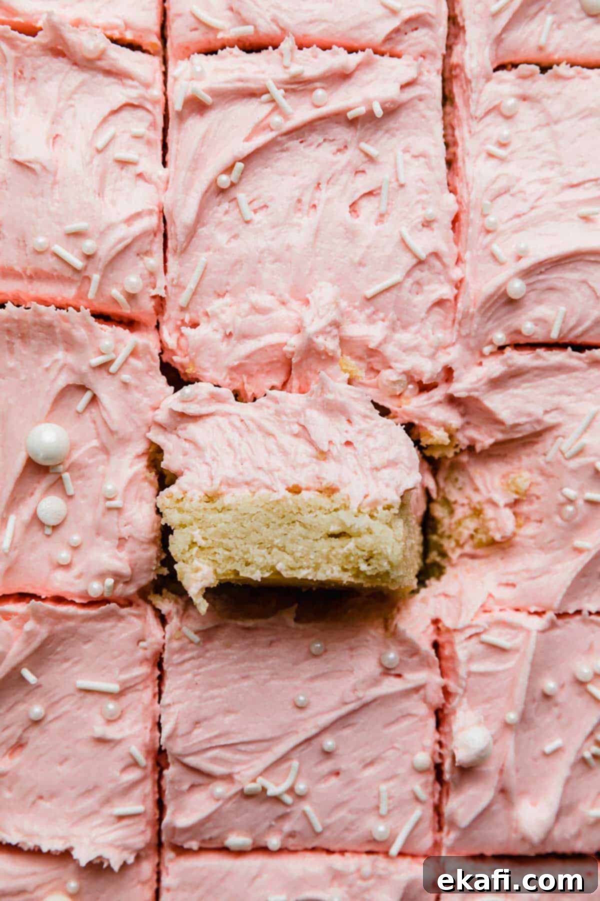 Frosted Sugar Cookie Bars 8 Sugar cookie bars cut into squares, topped with a swirl of pink frosting, beautifully presented.