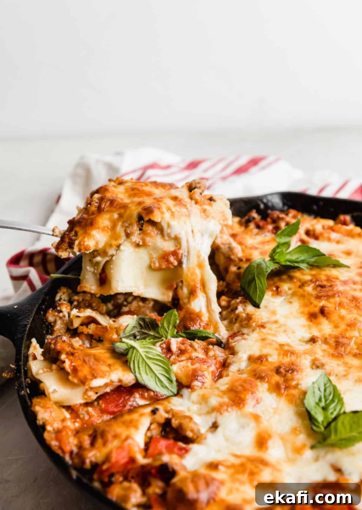 Rustic Cast Iron Lasagna 2 A spoon scooping out Cast Iron Lasagna noodles from a black skillet.