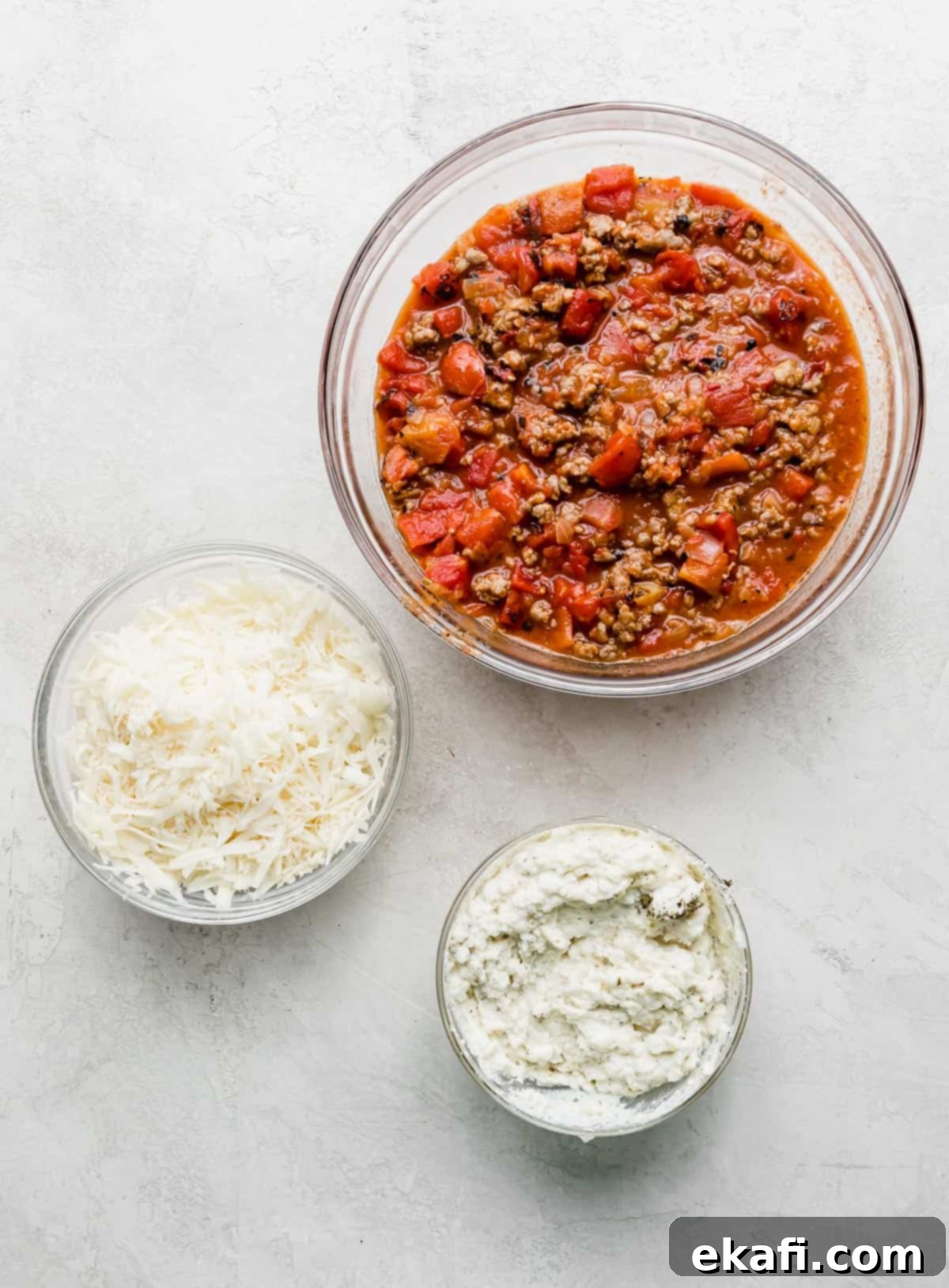Rustic Cast Iron Lasagna 4 Three bowls one with a red tomato and meat mixture, one with mozzarella cheese, and another with an herb ricotta mixture; all are used to make cast iron lasagna.