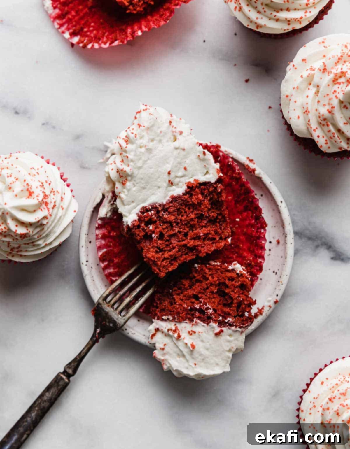 Crimson Velvet Delights 7 A Red Velvet Cupcake cut in half, on a white plate that's on a white marble table.