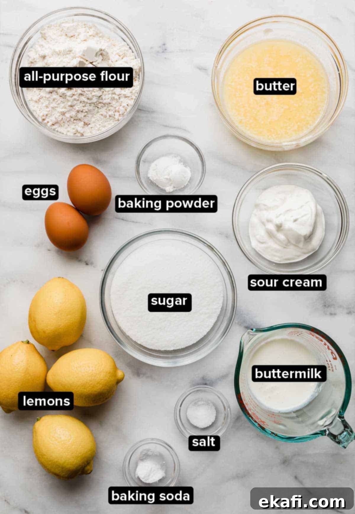 Zesty Lemon Cupcakes 3 Lemon Cupcake ingredients portioned into glass bowls on a white marble background.