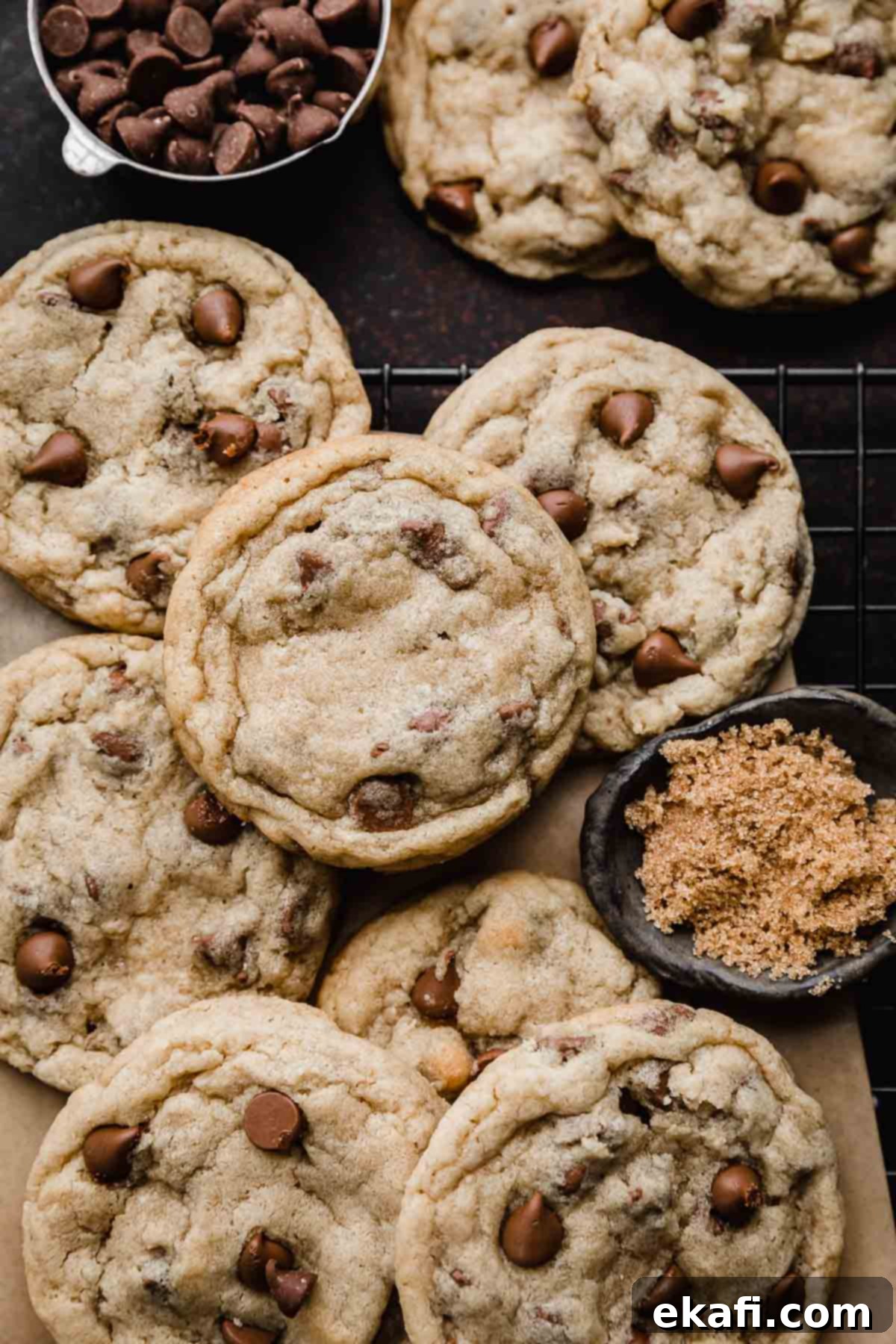 Irresistible Milk Chocolate Chip Cookies 2 Freshly baked Milk Chocolate Chip Cookies cooling on a black wire rack, with a small bowl of brown sugar and milk chocolate chips nearby.
