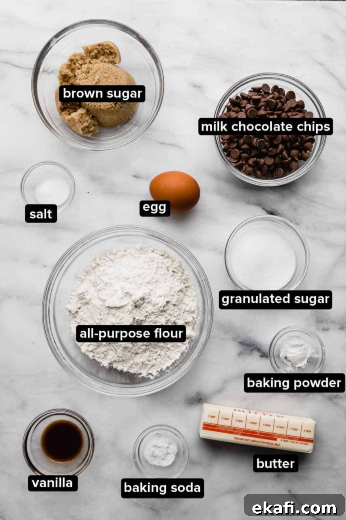 Irresistible Milk Chocolate Chip Cookies 3 Portioned ingredients for Milk Chocolate Chip Cookies displayed in glass bowls on a white marbled background.