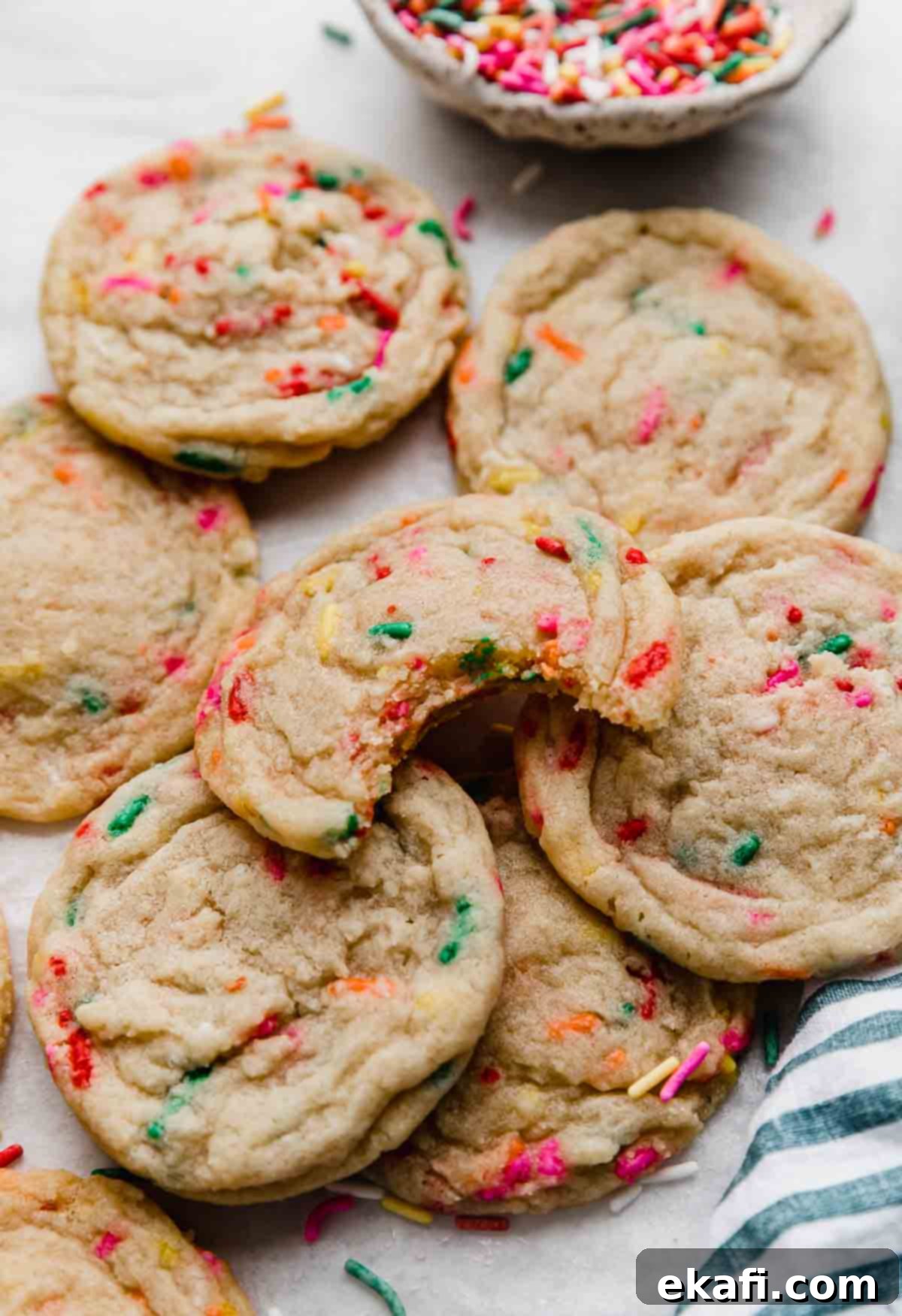 Celebration Cookies 2 A stack of soft and chewy Funfetti Cookies, with one cookie having a bite taken out, showcasing its vibrant rainbow sprinkles and tender interior.