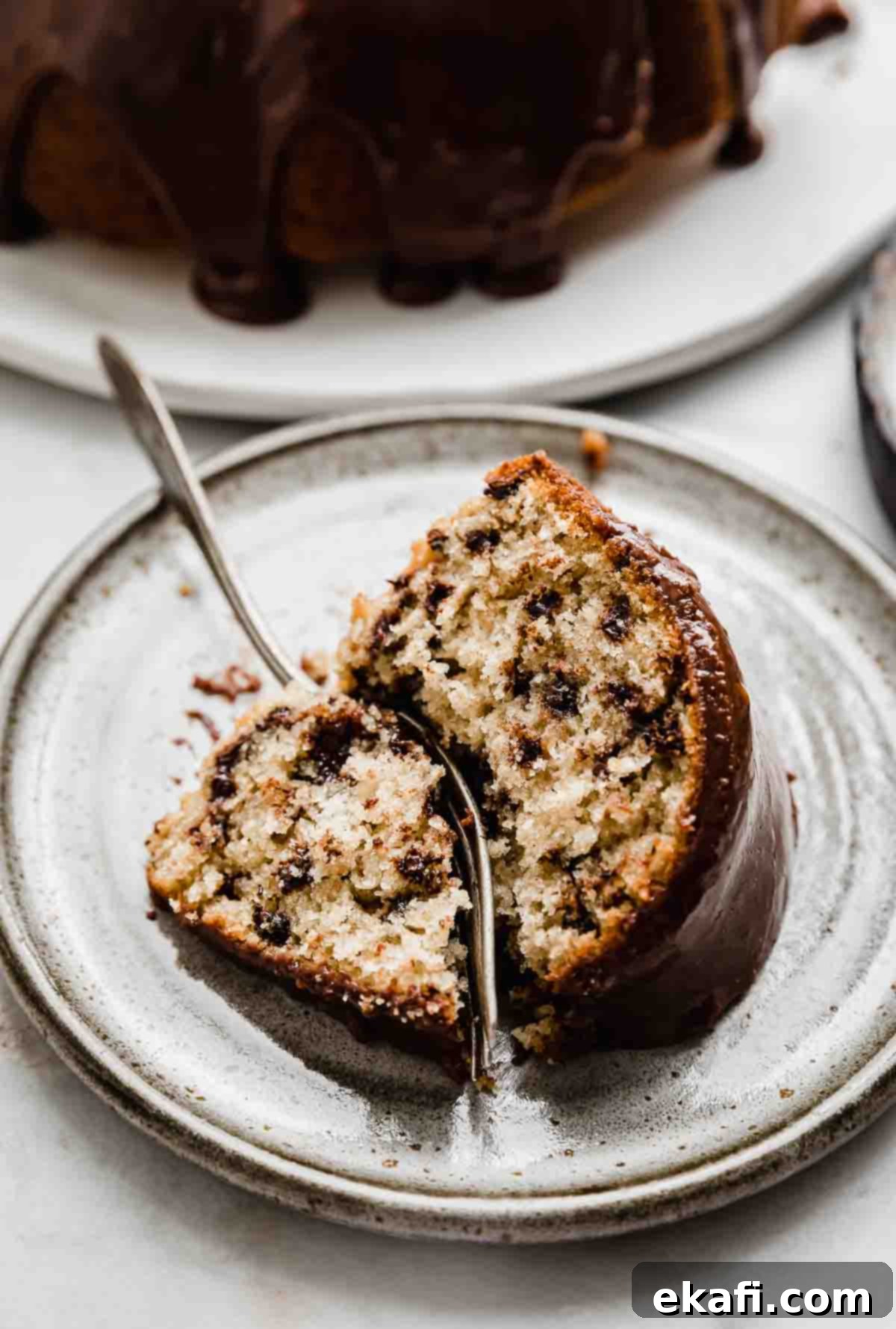 Rich Chocolate Chip Bundt Perfection 6 A slice of Chocolate Chip Bundt Cake on a gray plate with a fork cutting into the cake, showing its soft and inviting interior.