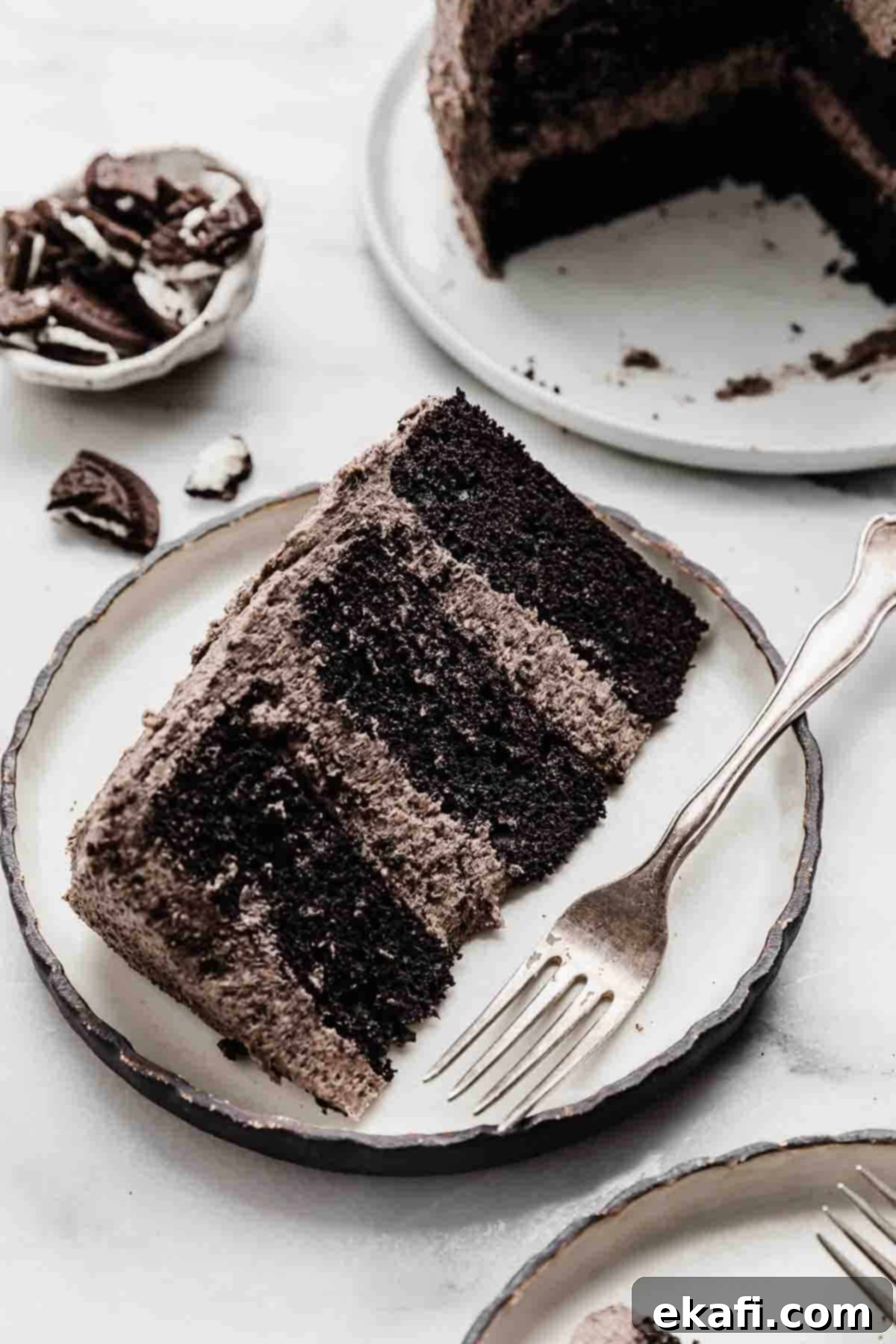 Decadent Oreo Dream 3 A slice of three layer Oreo Cake frosted with an Oreo frosting, on a black rimmed white plate.