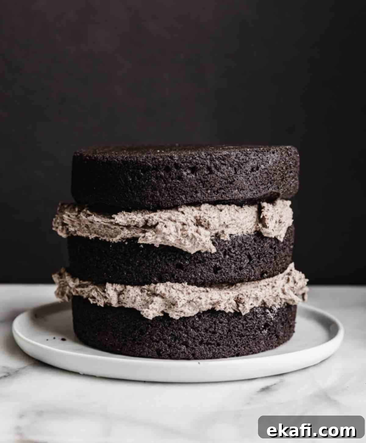 Decadent Oreo Dream 5 A three layer black cocoa cake with Oreo frosting between each cake layer, against a white background.