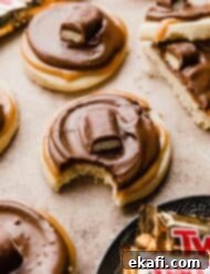 Τουίξ Μπισκότα 7 Μπισκότα Twix φτιαγμένα με βάση μπισκότου βουτύρου, επικαλυμμένα με καραμέλα, σοκολάτα και μια μπάρα Twix, σε ανοιχτό καφέ φόντο.