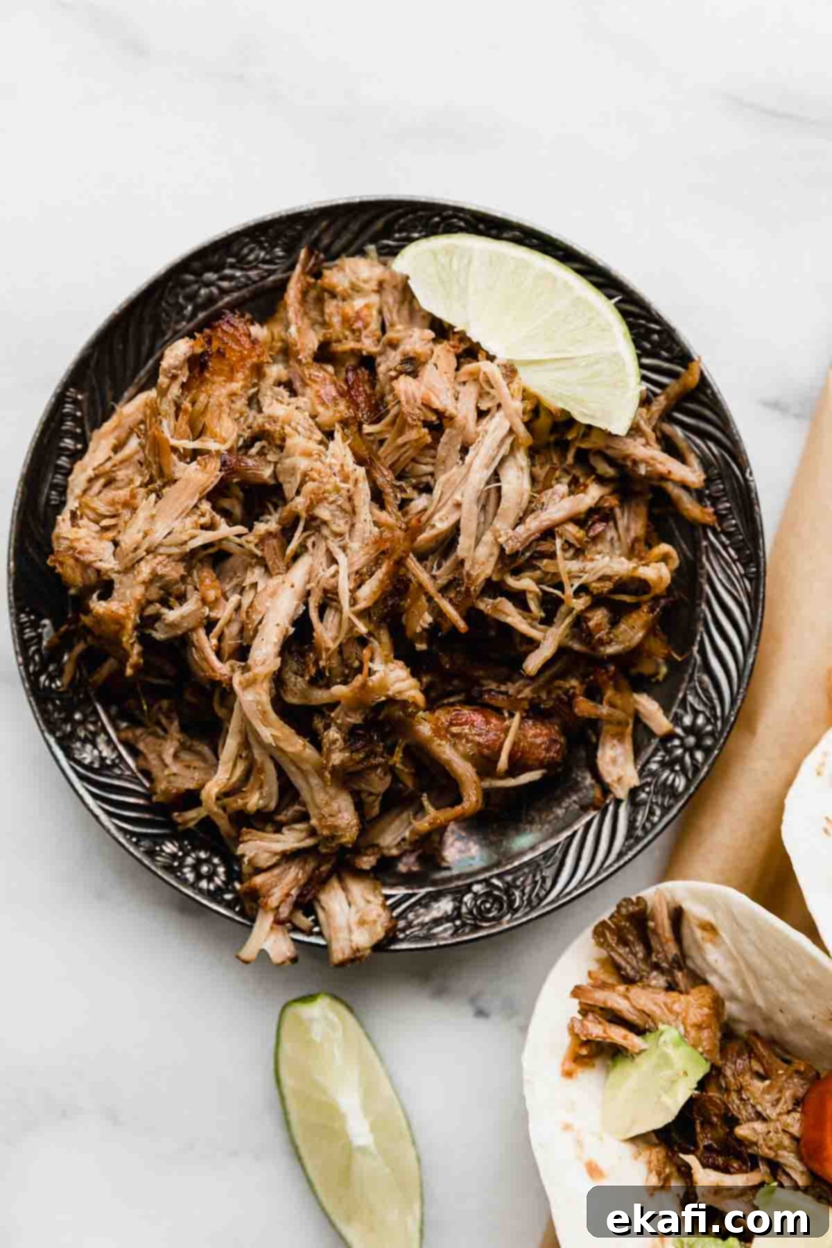 Carnitas 6 Slow cooker Mexican shredded pork on a black plate on a white background.