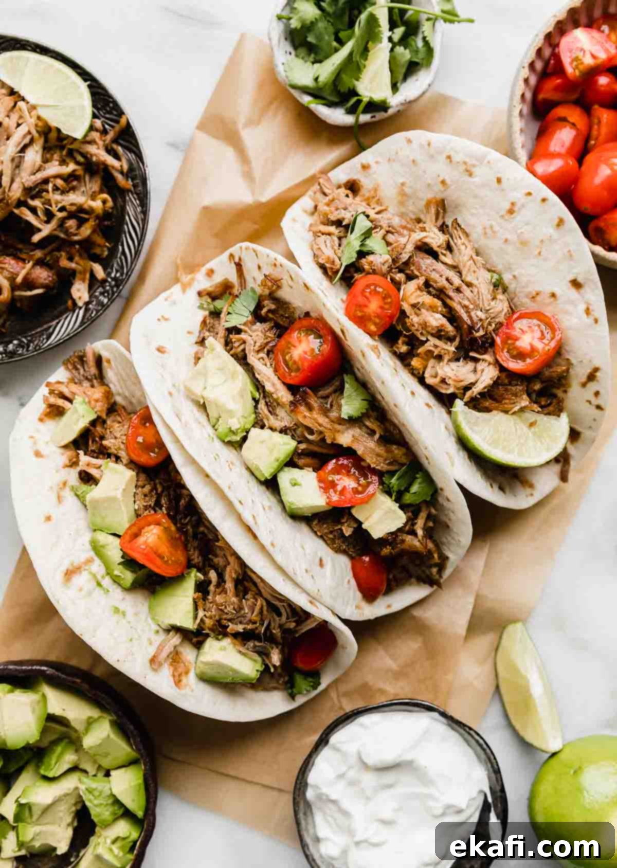 Carnitas 7 Carnitas on a Kraft colored parchment paper on a white background with avocado and tomatoes surrounding the carnitas.