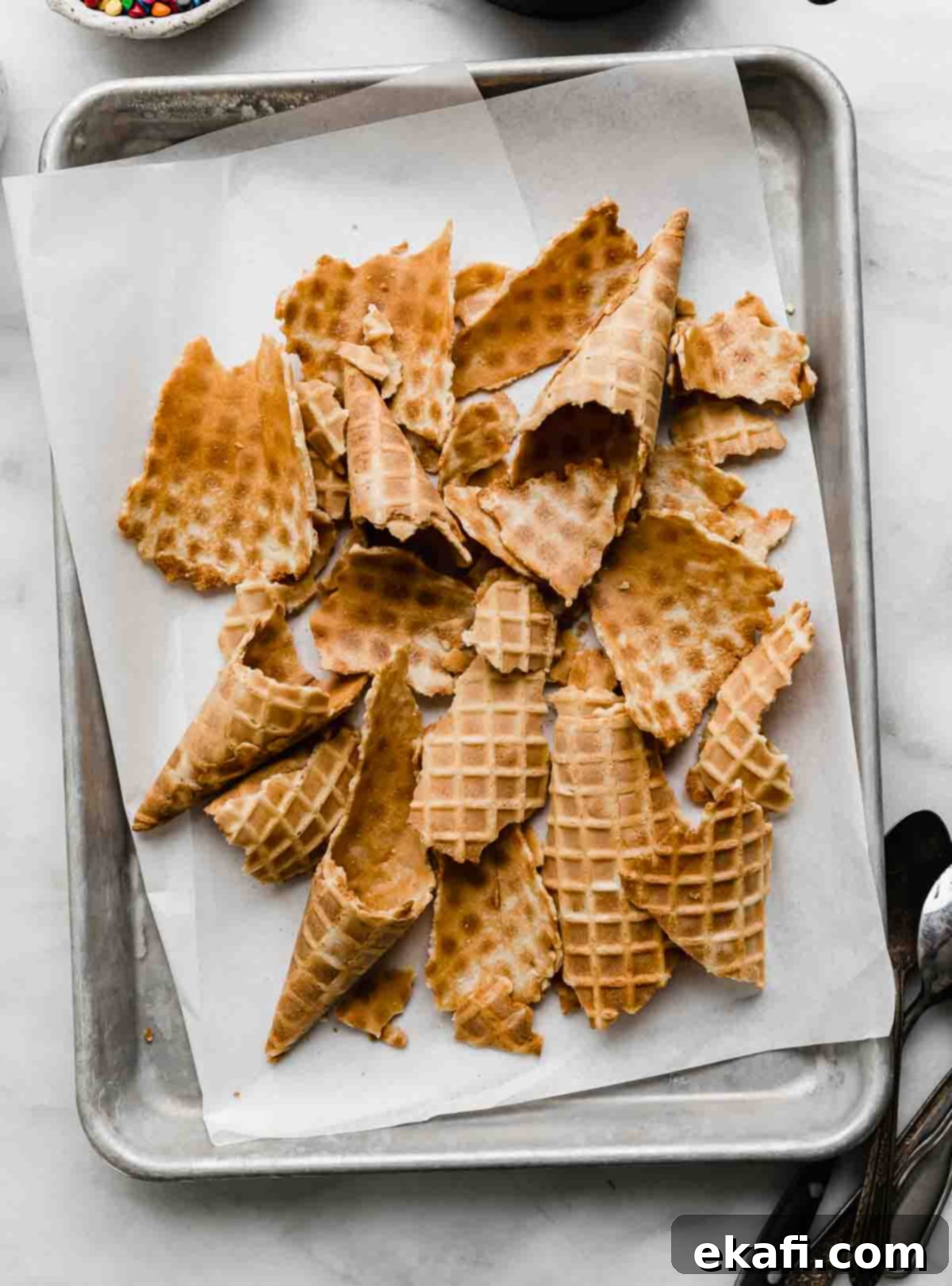 The Sweet Scoop Fiesta 4 Broken waffle cones on a white parchment lined baking sheet on a white background.