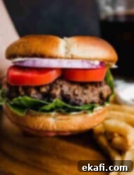 Μπέργκερ Μπριζόλας 7 Ένα ψωμάκι burger με ντομάτα, μοβ κρεμμύδι και μαρούλι, με ένα μεγάλο μπιφτέκι Steakhouse Burgers σε σκούρο καφέ φόντο.