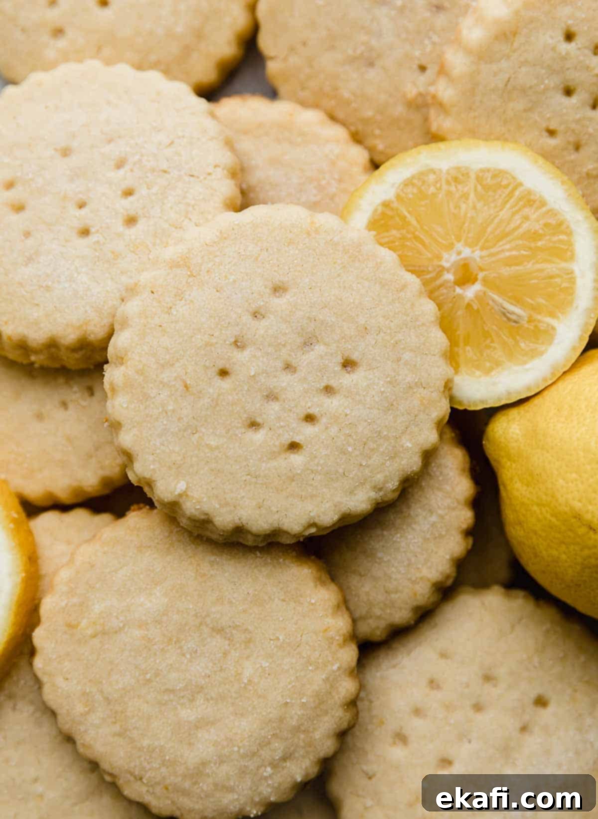 Sunshine Lemon Shortbread 2 A close up photo of Lemon Shortbread Cookies stacked on top of each other, with a lemon slice to the right of the cookies.