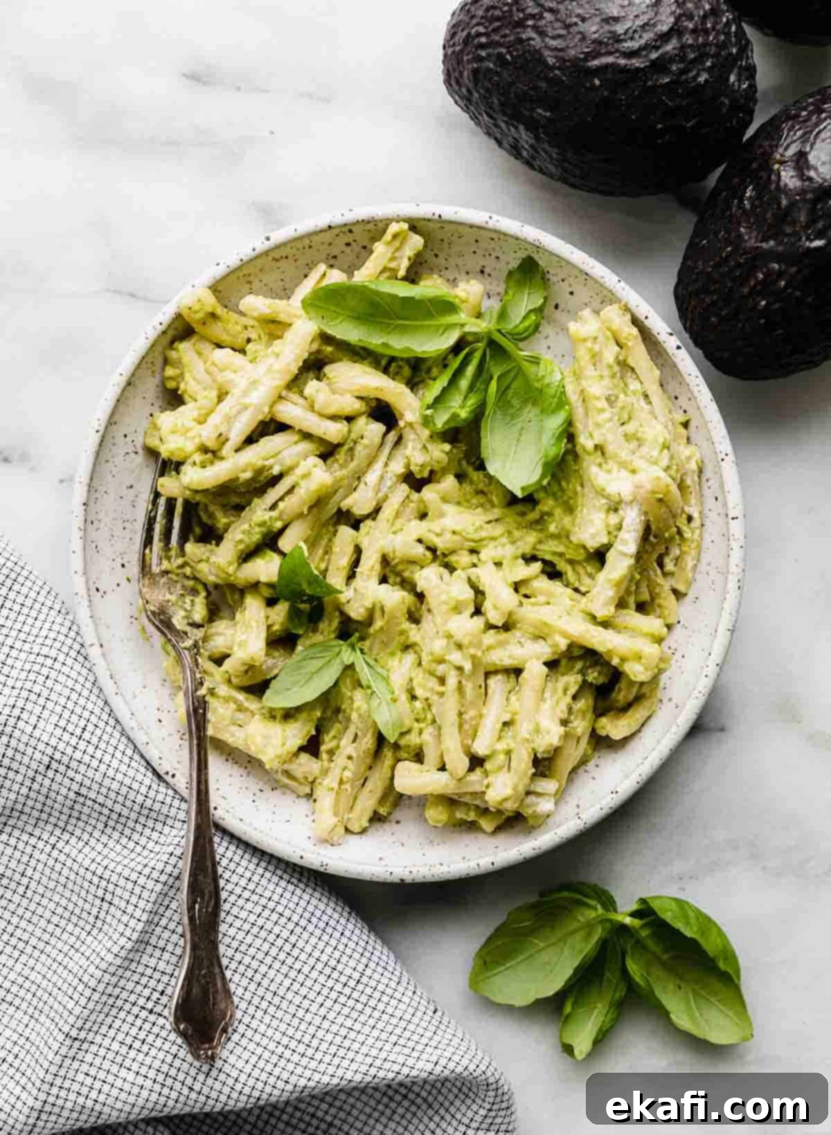 Vibrant Avocado Pesto Pasta 2 Avocado Pesto Pasta in a white bowl on a white background, garnished with fresh basil leaves.
