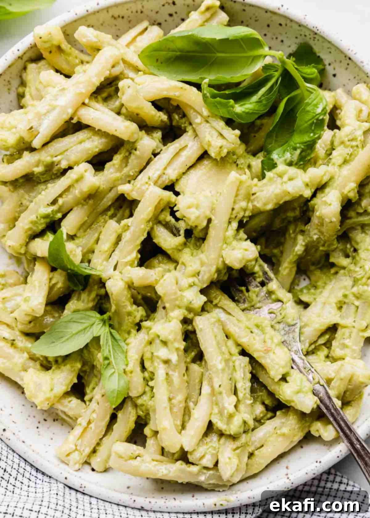 Vibrant Avocado Pesto Pasta 5 A close up image of pasta tossed in a light green basil pesto with mashed avocado and topped with fresh basil leaves.