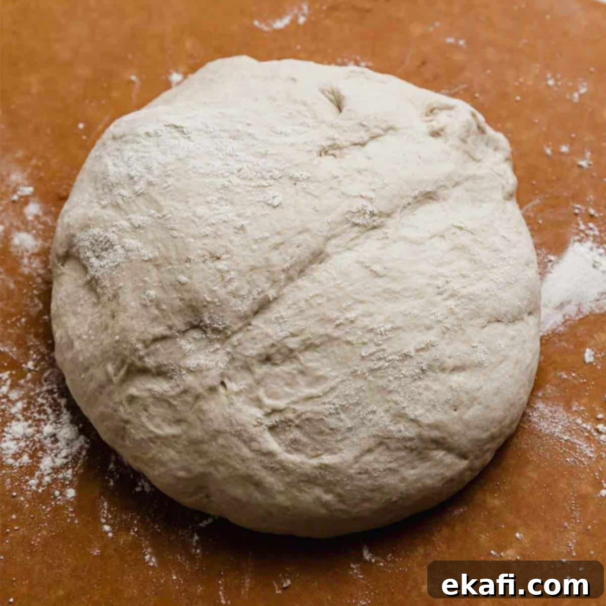 Flawless Pizza Dough Every Time 5 A perfectly risen ball of homemade pizza dough on a rustic wooden background.