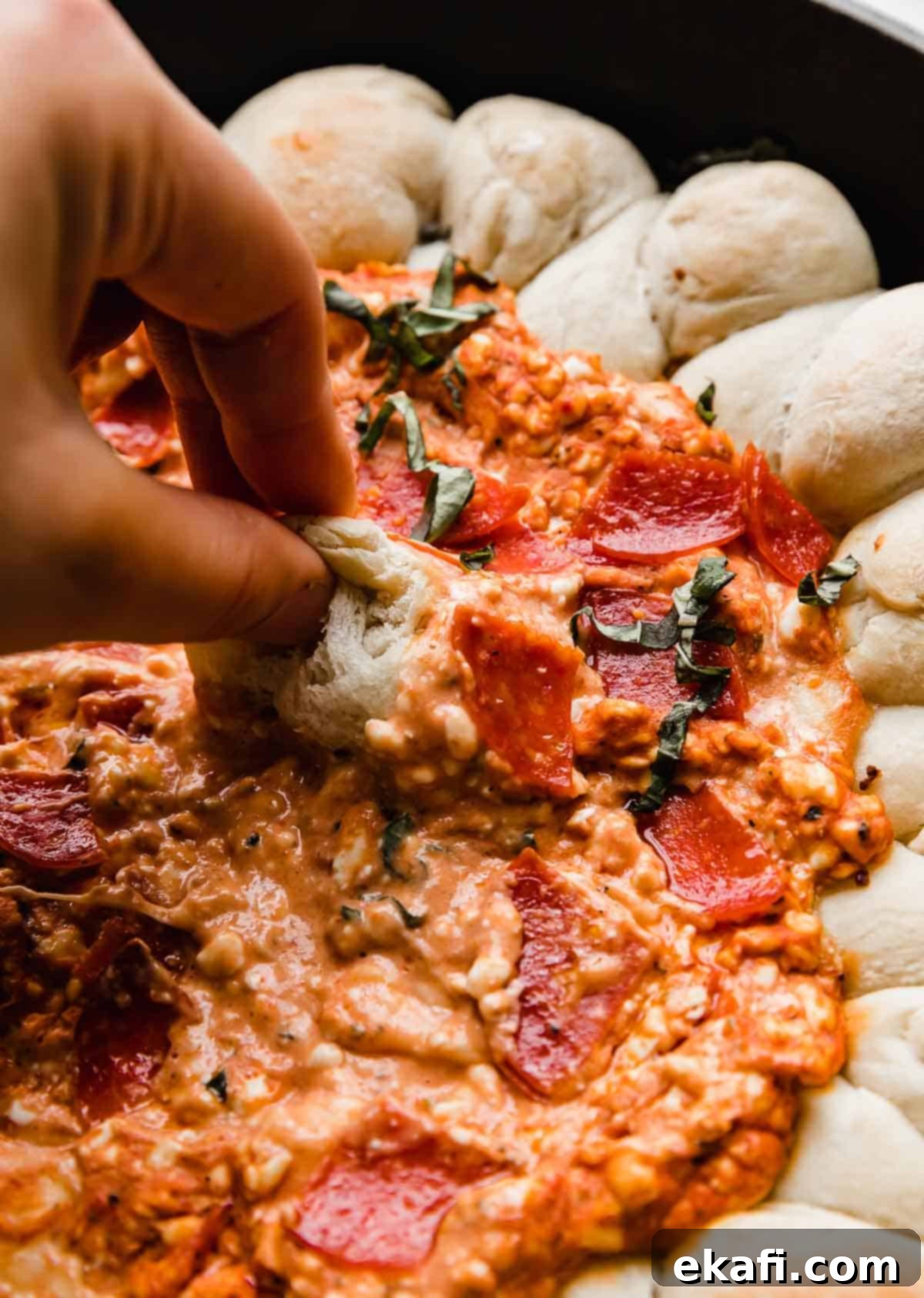 Ultimate Pepperoni Pizza Dip 6 A golden brown, baked pizza roll being dipped into a luscious, stringy, and cheesy cream cheese pizza dip, highlighting the delightful texture of both components.