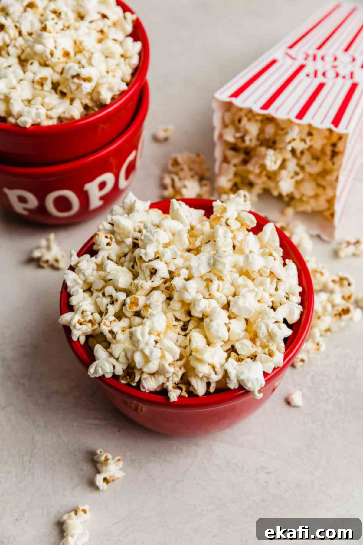 Sweet and Salty Kettle Corn 2 Kettle Corn Popcorn in a red bowl on a light gray background, with kettle corn surrounding the bowl.