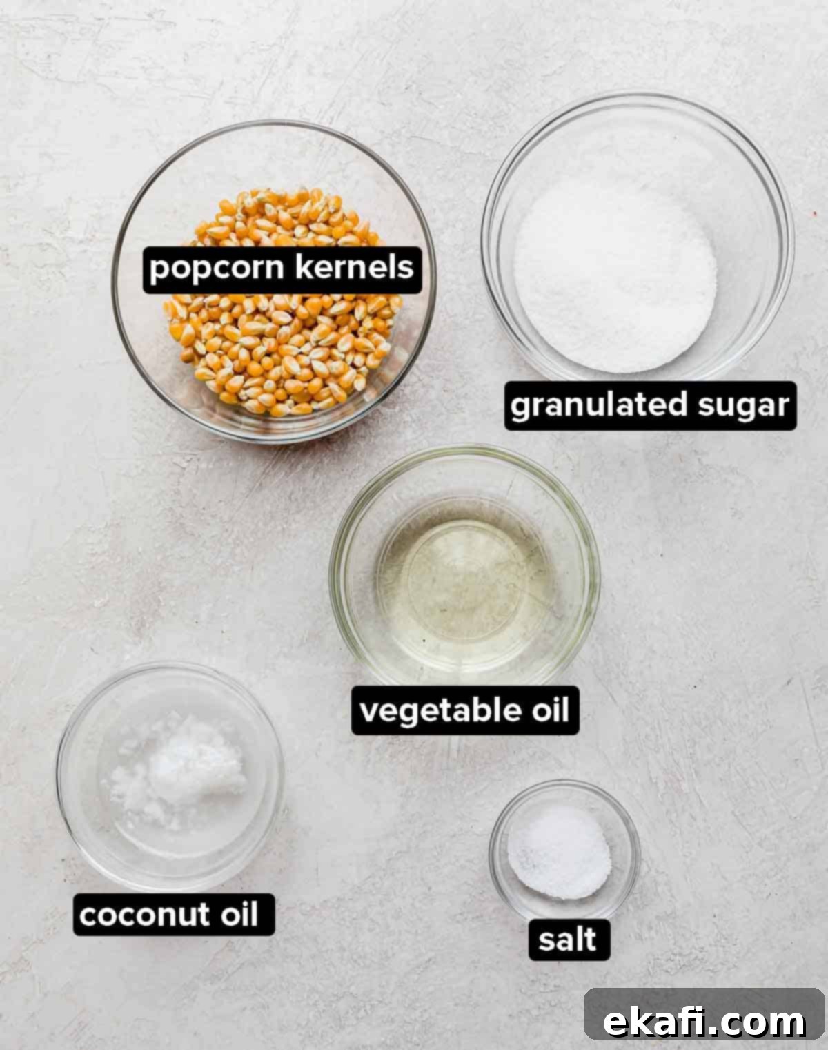 Sweet and Salty Kettle Corn 3 Kettle Corn Popcorn ingredients on a light gray textured background: vegetable oil, coconut oil, popcorn kernels, salt, and granulated sugar.