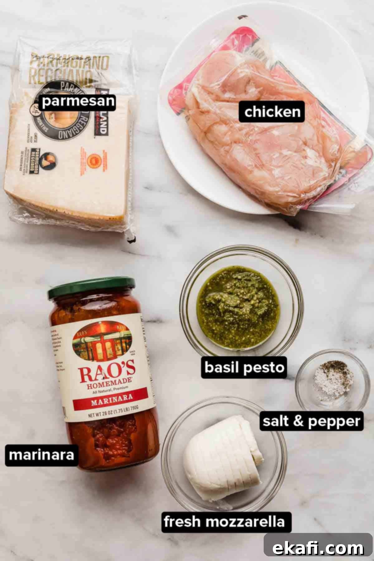 Pesto Parmesan Chicken 3 Pesto Chicken Parmesan ingredients on a white marble table, parmesan, chicken, marinara, pesto, mozzarella, salt and pepper.