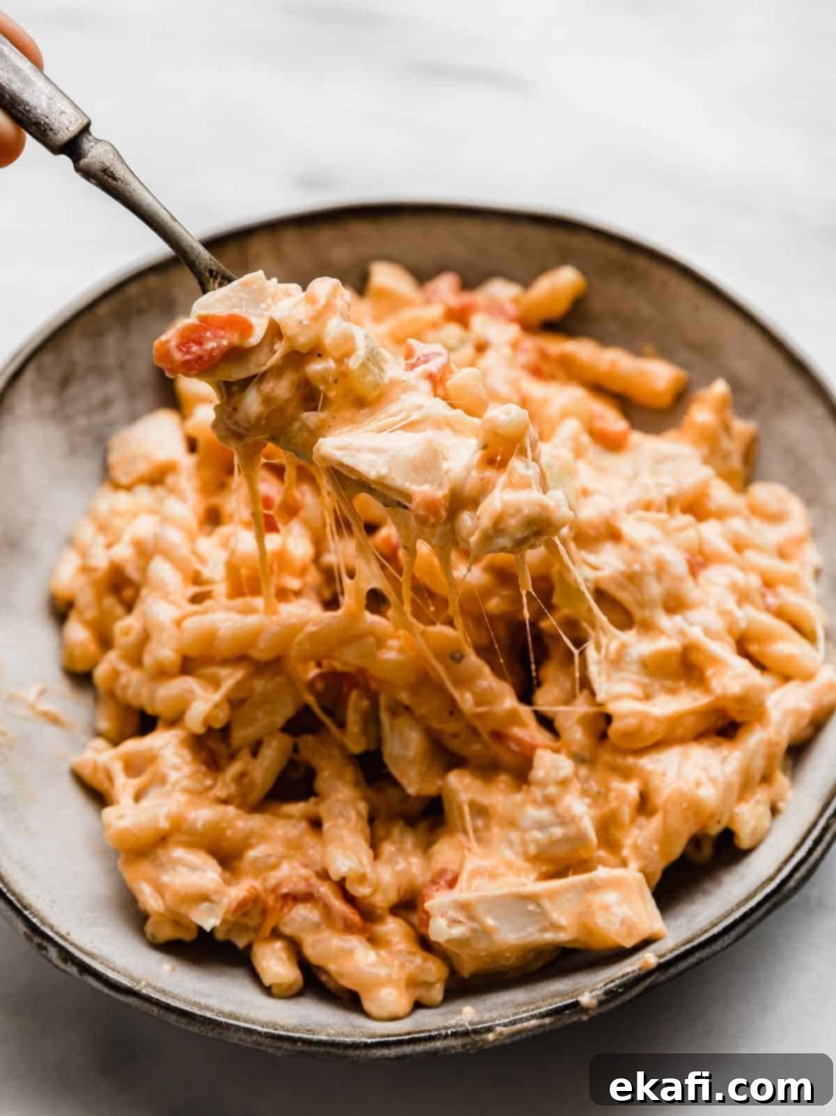 Ultimate Buffalo Chicken Pasta 2 A gray bowl filled with cheesy Buffalo Chicken Pasta and a fork pulling up some of the pasta to show how cheesy it is.