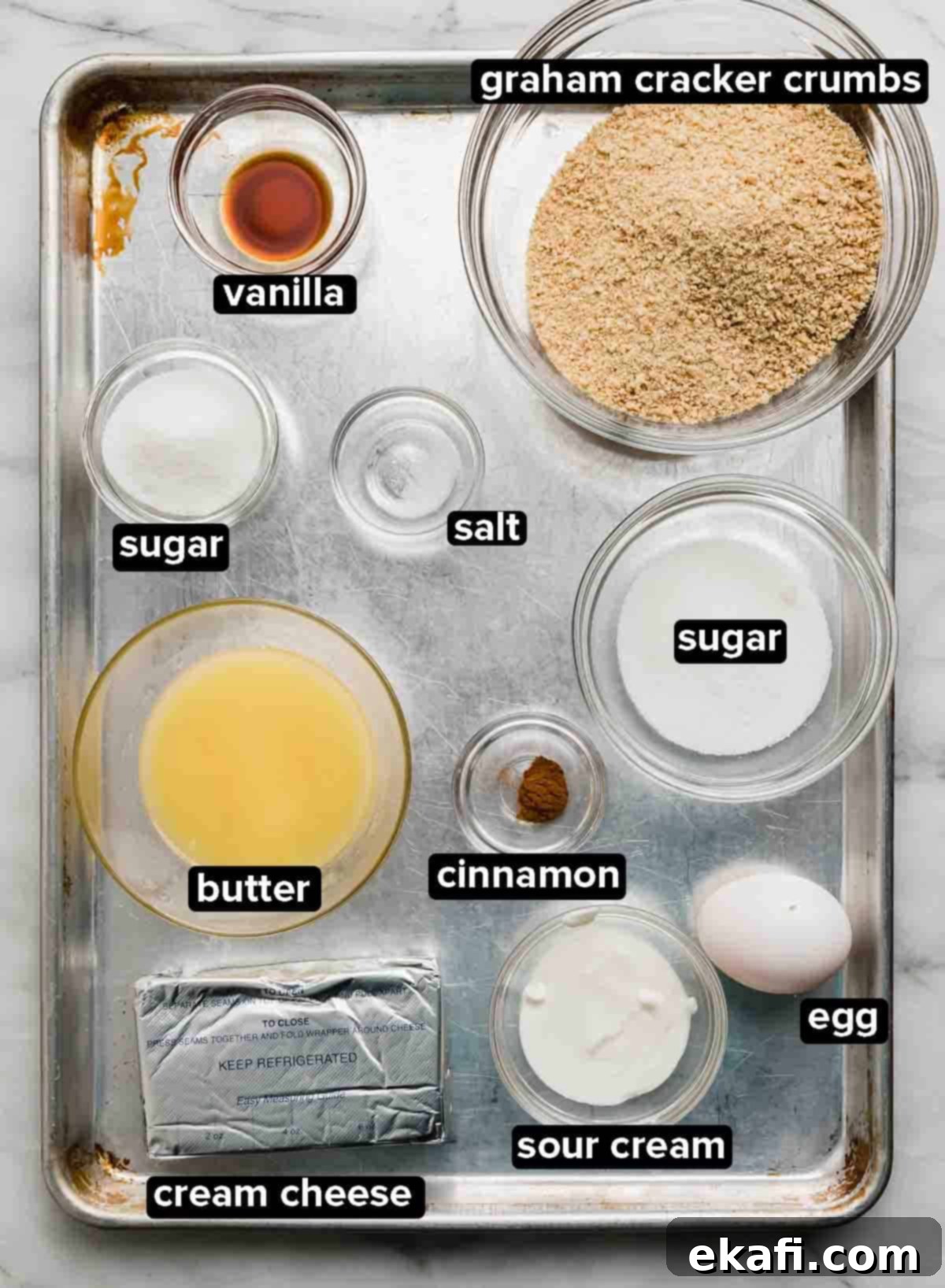 Bite-Sized Cheesecakes 3 Ingredients used to make the best Mini Cheesecakes recipe portioned into glass bowls on a silver baking sheet: graham cracker crumbs, butter, sugar, egg, vanilla, and cream cheese.