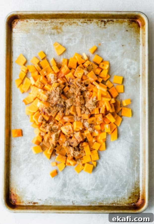This Cinnamon Roasted Butternut Squash will be your new favorite fall side dish. The butternut squash melts in your mouth! Cubed butternut squash piled in the middle of a baking sheet with brown sugar, cinnamon, and salt sprinkled overtop.