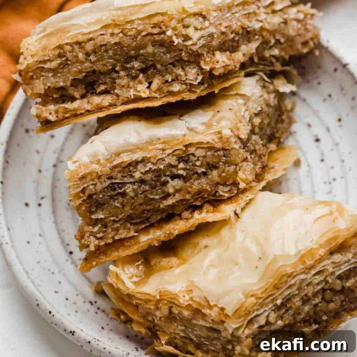 Authentic Greek Baklava 2 Three golden, diamond-shaped Greek Baklava pastries resting on a pristine white plate, showcasing their flaky layers and honey glaze.