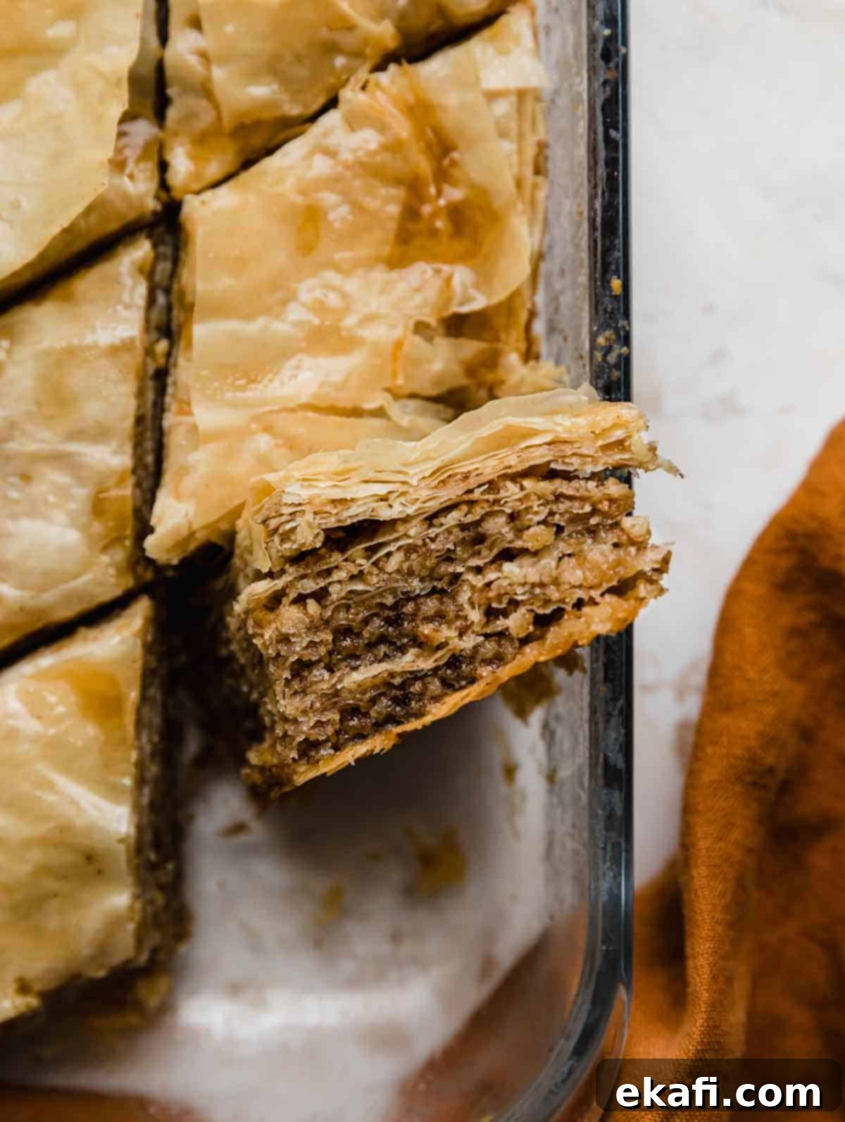 Authentic Greek Baklava 8 A piece of flaky Greek Baklava, cut into a diamond shape, is turned on its side to reveal the intricate interior layers of phyllo dough and the rich, crushed walnut filling, showcasing the perfect texture of this traditional baklava recipe.