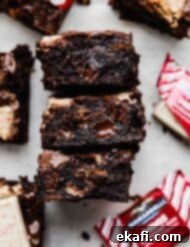 Μπράουνις με Κρουστά Σοκολάτας Μέντας 7 Peppermint Bark Brownies σε λευκό φόντο με μερικές κόκκινες συσκευασίες σοκολάτας μέντας Ghirardelli κοντά στα brownies.