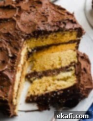 Golden Cake with Decadent Chocolate Frosting 9 A slice of yellow cake topped with chocolate frosting on a white cake plate.