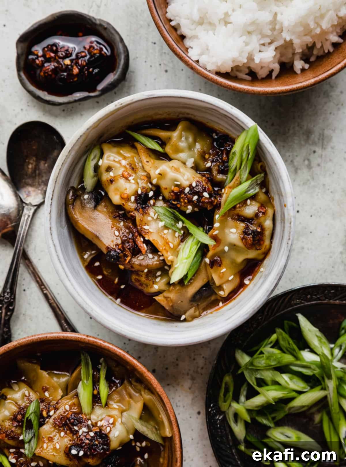 Πικάντικα Γουόντον Κοτόπουλου 5 Πικάντικα Wontons Κοτόπουλου γαρνιρισμένα με κομμένα φρέσκα κρεμμυδάκια σε ένα λευκό μπολ σε ανοιχτό γκρι φόντο.