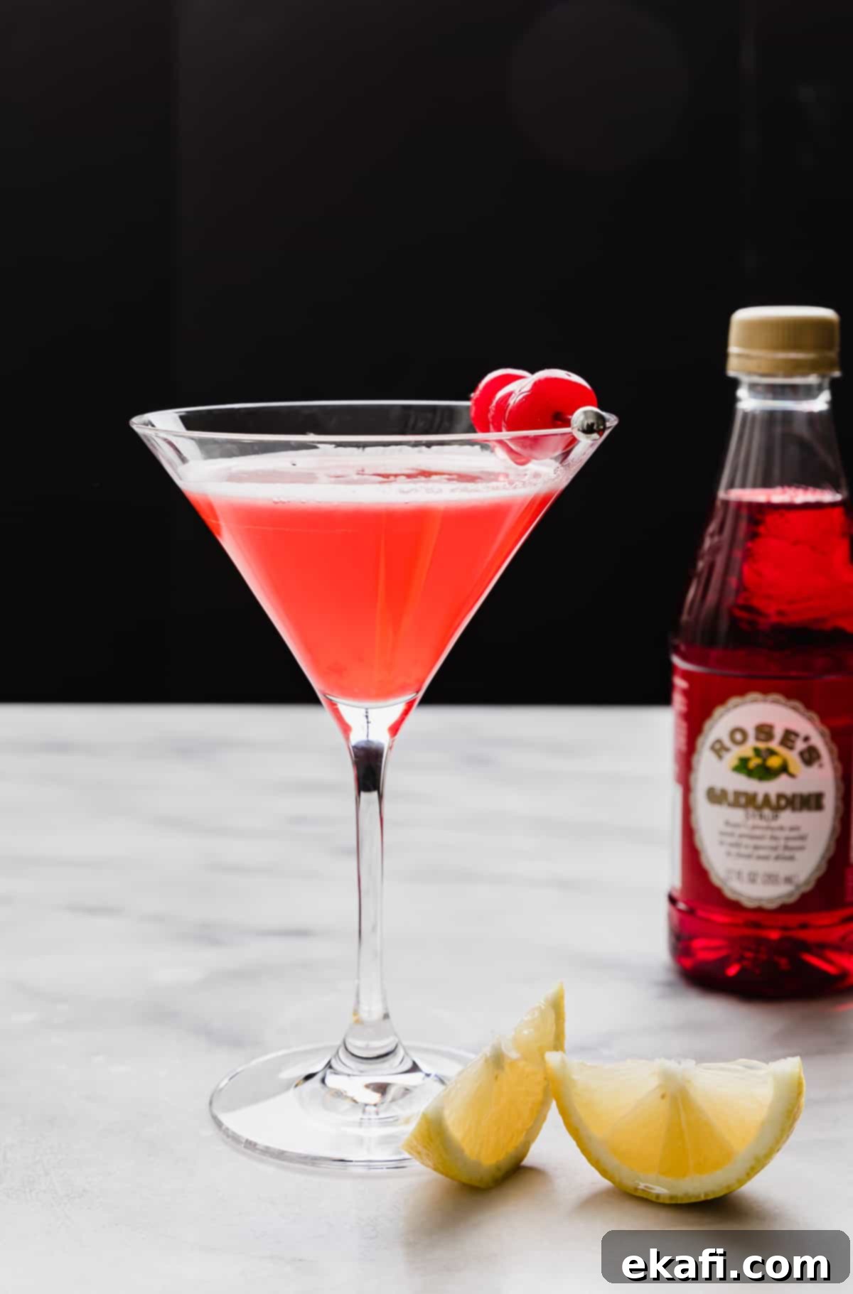 Pink Lady Bliss 2 A martini glass filled with a bright Pink Lady Mocktail and garnished with maraschino cherries, against a black background.