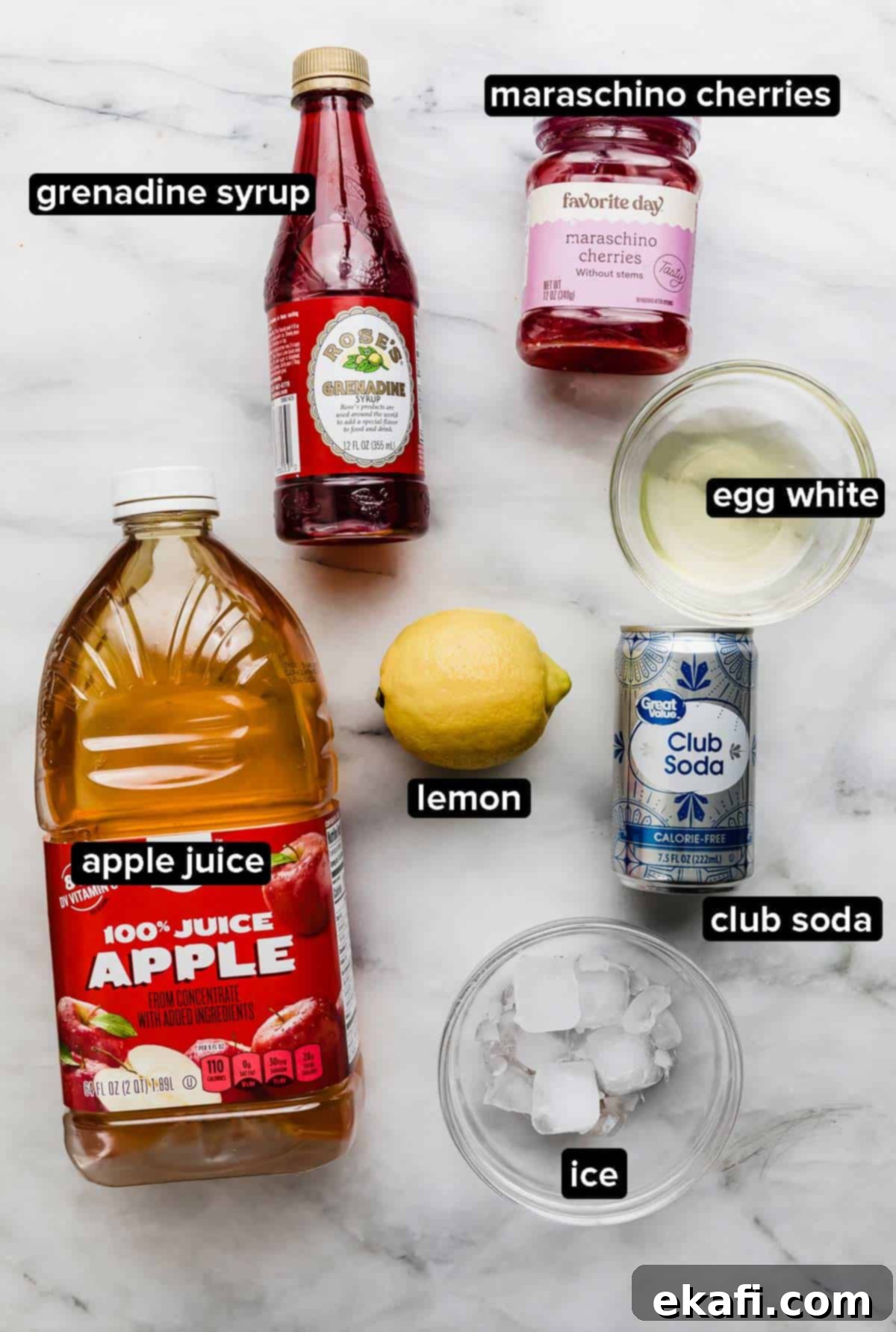 Pink Lady Bliss 3 Pink Lady Mocktail ingredients on a white marble background: grenadine syrup, egg white, lemon, apple juice, club soda, ice, and maraschino cherries.