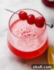 Pink Lady Bliss 7 Pink Lady Mocktail in a small glass with three maraschino cherries on a cocktail stick.