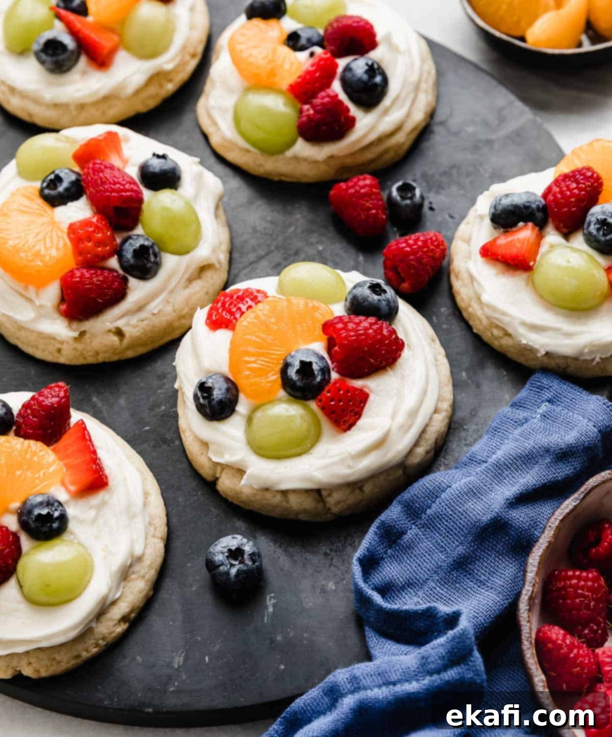 Fruity Dessert Cookie Pizzas 2 Fruit Pizza Cookies topped with a cream cheese frosting and topped with raspberries, blueberries, grapes, and mandarin oranges, showcasing their vibrant colors and appealing presentation.