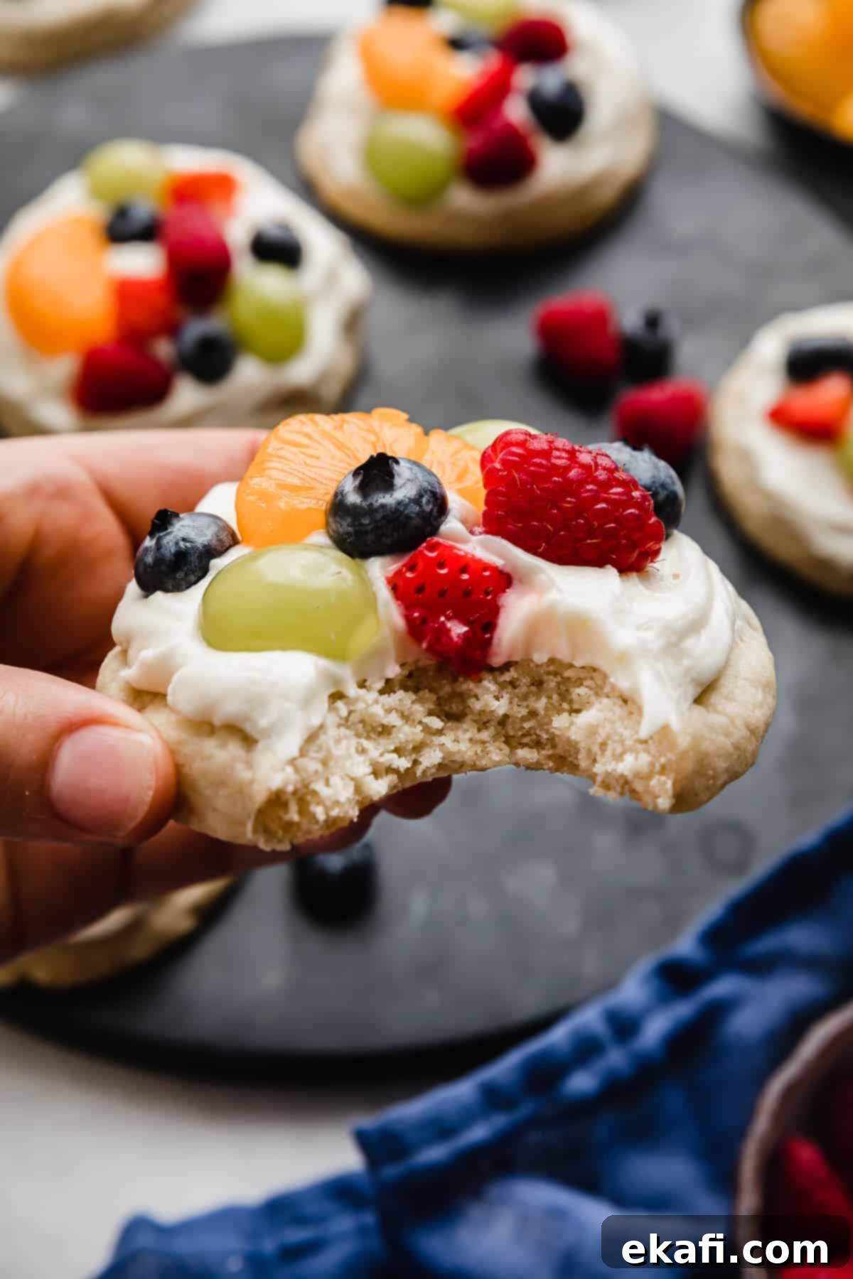 Fruity Dessert Cookie Pizzas 10 A hand gracefully holding the best Fruit Pizza Cookie, perfectly topped with creamy lemon cream cheese frosting and a medley of fresh, colorful fruits.