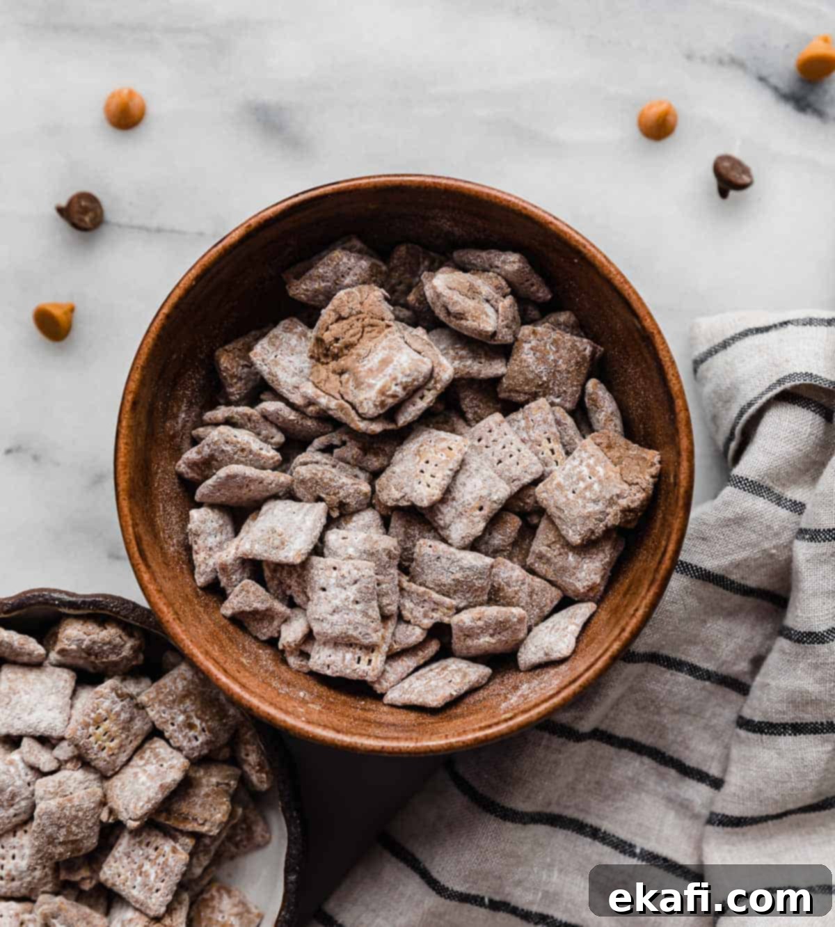 Butterscotch Cloud Crunch 2 A brown bowl filled with golden-brown Butterscotch Puppy Chow (chocolate butterscotch muddy buddies) dusted with powdered sugar, set on a bright white marble surface, ready to be enjoyed as a sweet and crunchy snack.