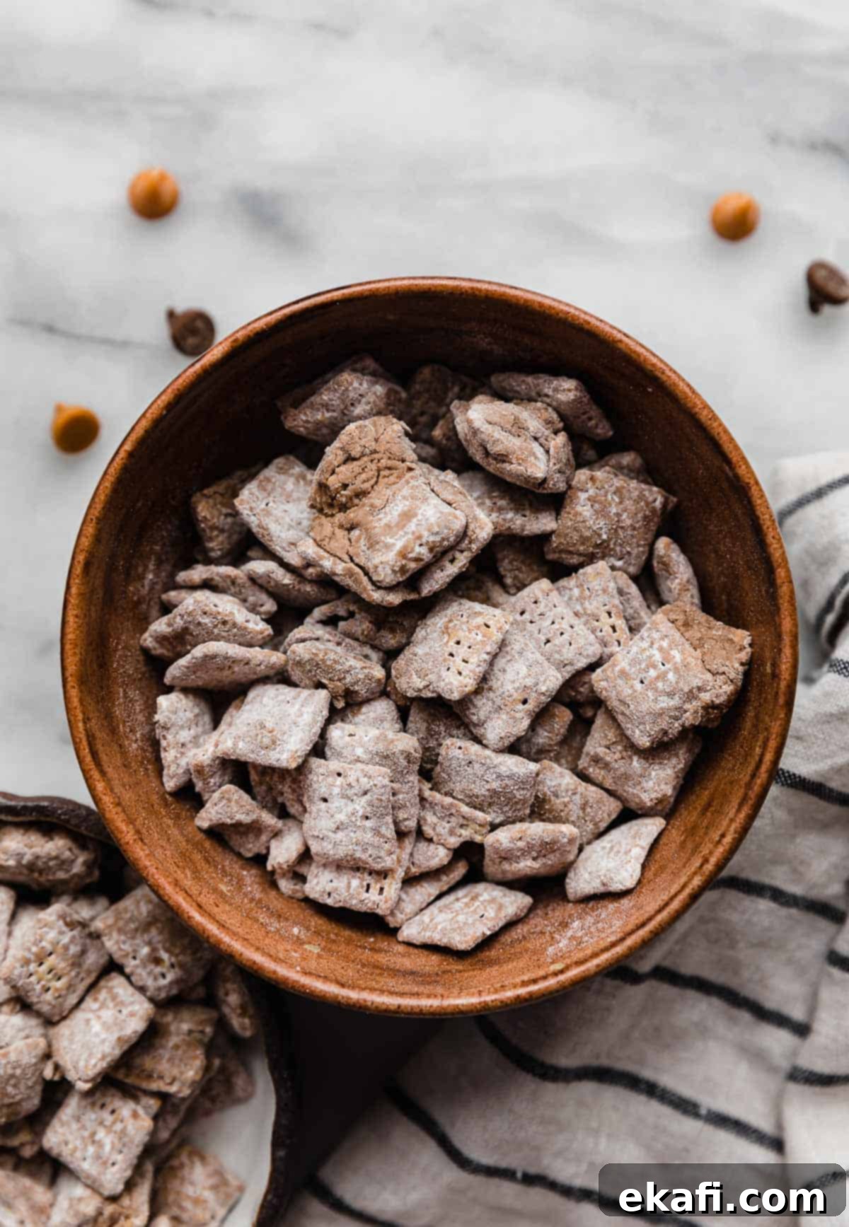 Butterscotch Cloud Crunch 6 A charming brown bowl overflowing with golden, powdered sugar-dusted Butterscotch Puppy Chow, arranged on a pristine white marble surface, highlighting the irresistible texture and vibrant colors of this homemade snack.