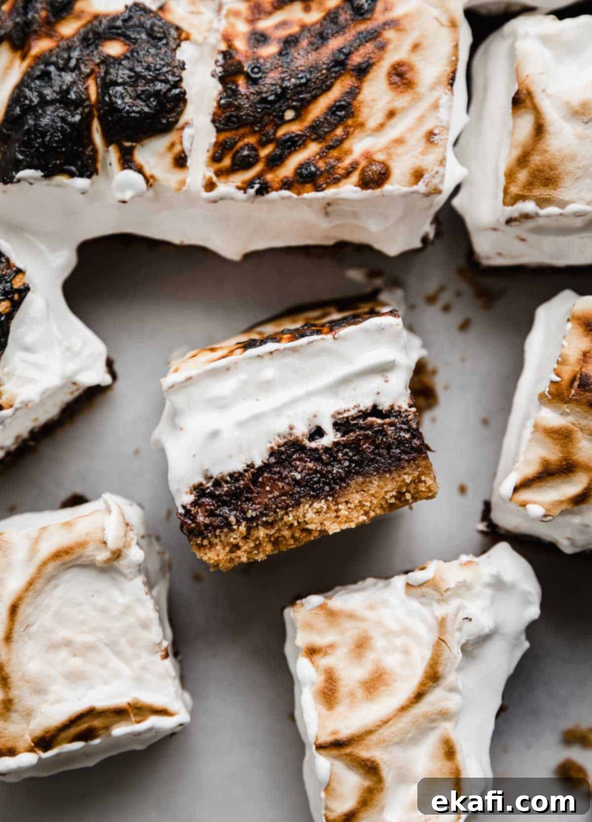 Μπράουνις Φωτιάς 2 S'mores Brownies κομμένα σε τετράγωνα, με ένα μπράουνι S'more στο πλάι να αναδεικνύει την κρούστα από μπισκότο graham, το ζουμερό μπράουνι και την σπιτική καβουρδισμένη κρέμα marshmallow από πάνω.