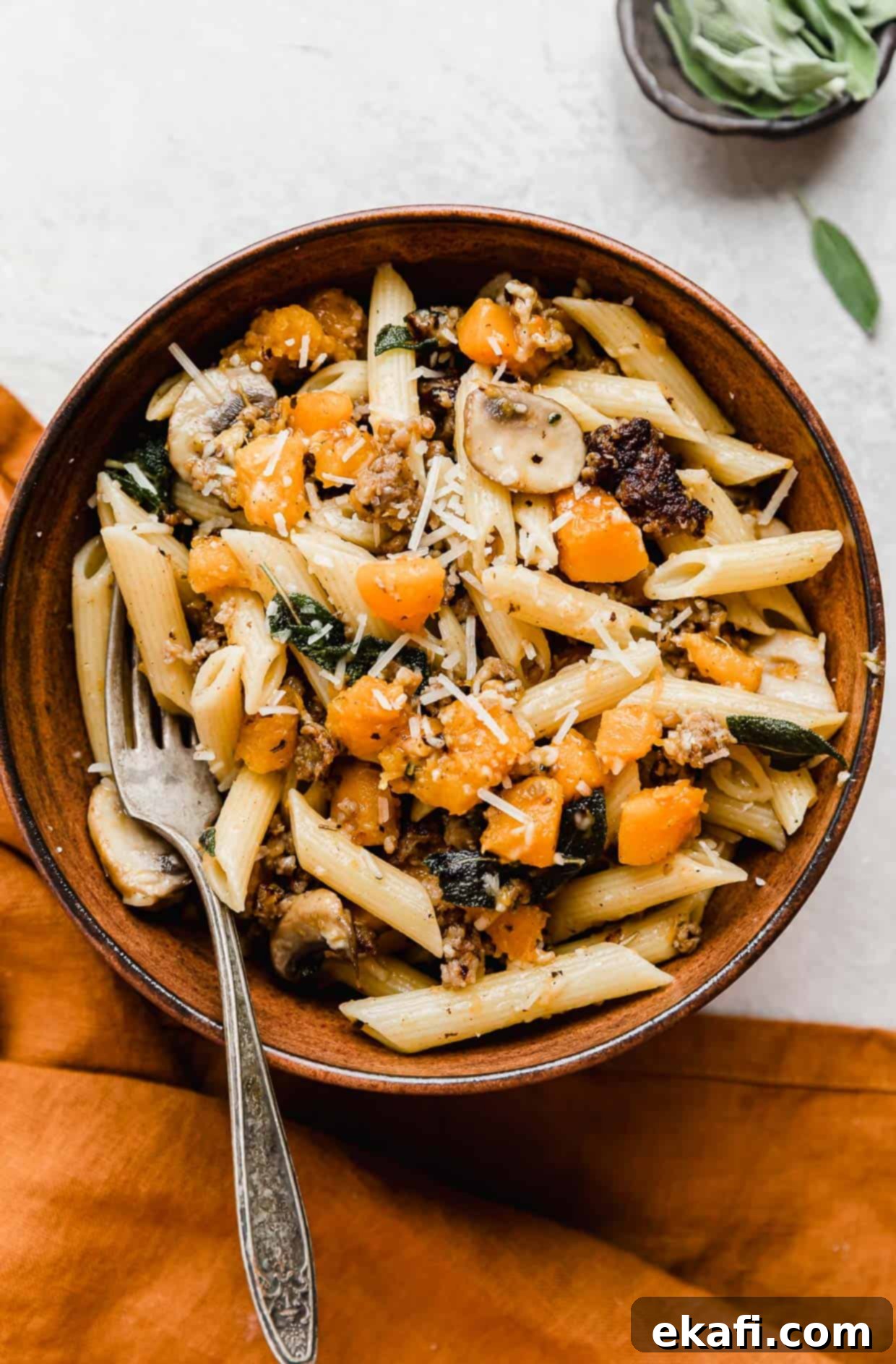Butternut Squash Sausage Pasta 2 A brown bowl with Butternut Squash Mushroom Pasta in it, garnished with fresh sage and parmesan cheese.