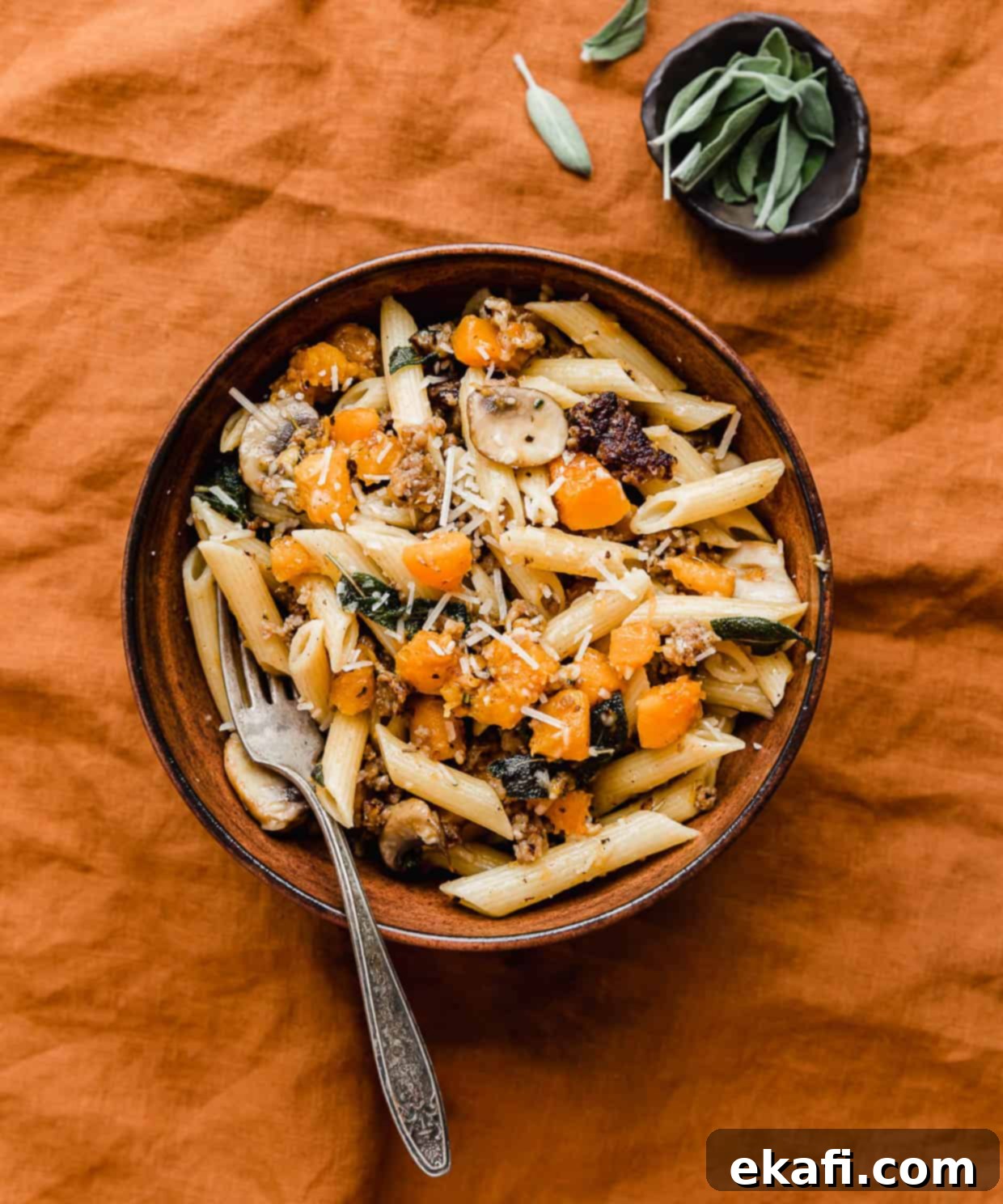 Butternut Squash Sausage Pasta 6 Butternut Squash Mushroom Pasta in a brown bowl on a burnt orange linen napkin, ready to be served.